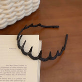 Zigzag Hair Band – Flexible Plastic Headband resting on a book, highlighting its durable black design.